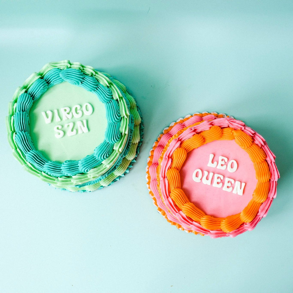 Two Round ornate astrology cakes. One teal and green and one pink and orange.