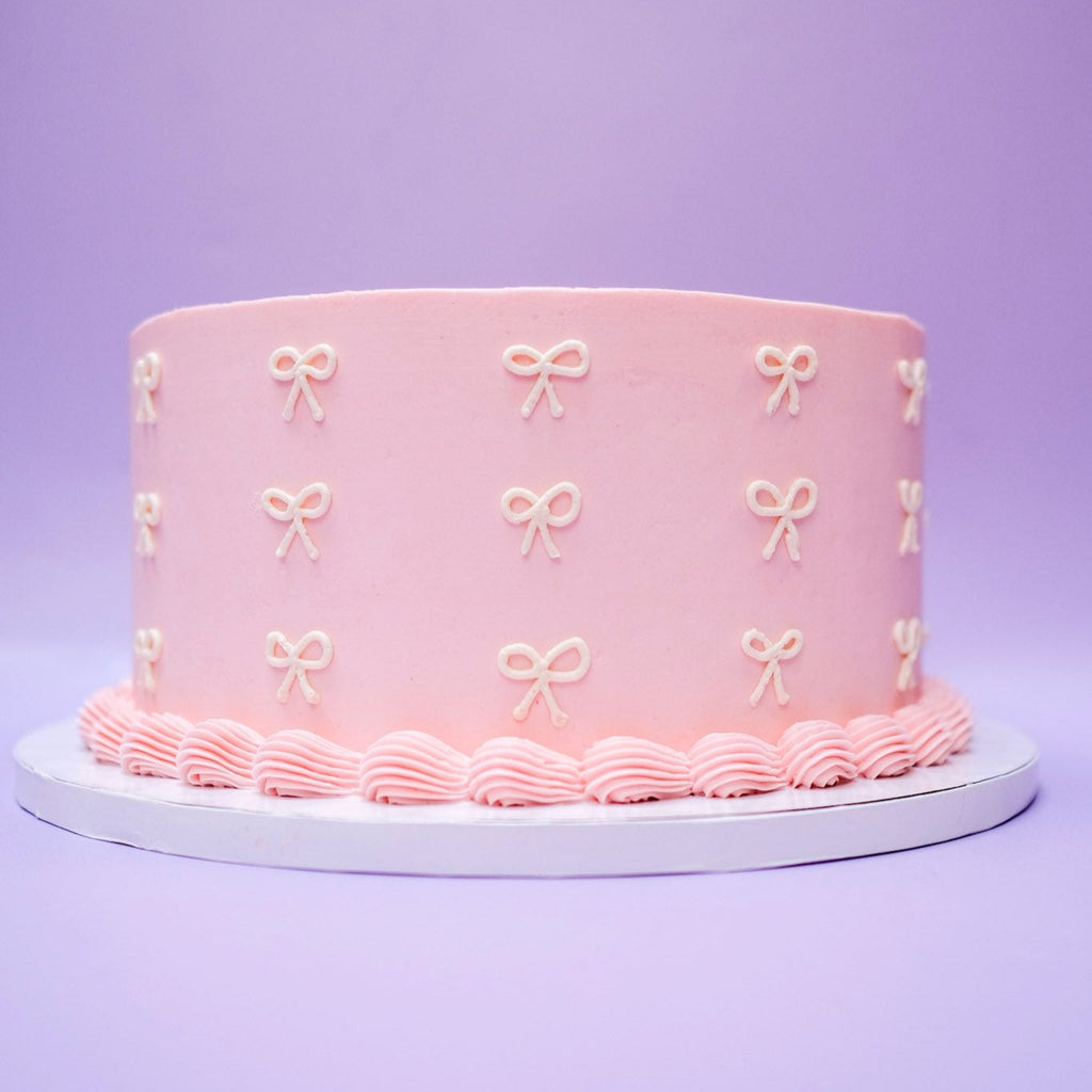A pink cake with pink piping and white ribbon. 