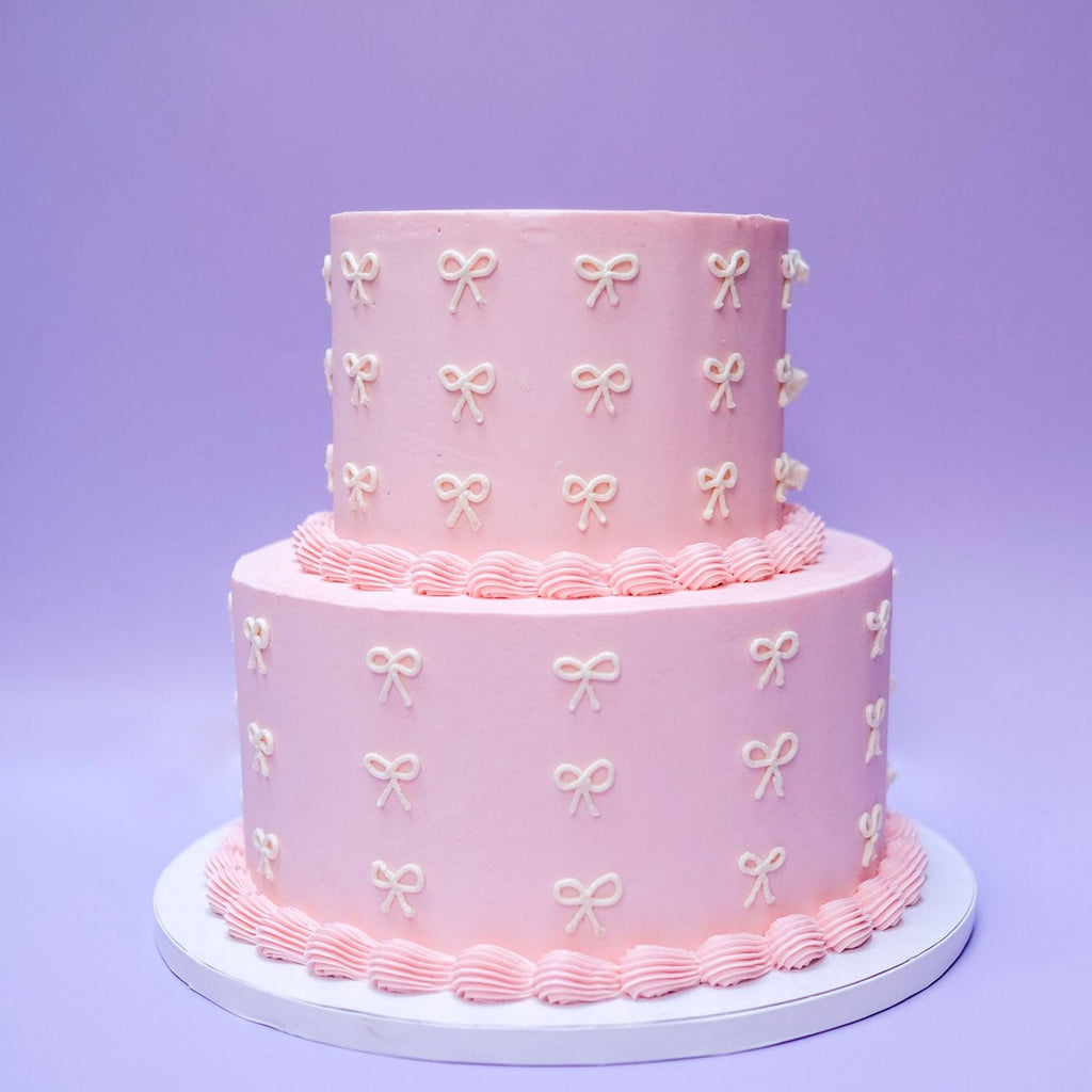 A two tiered pink cake with pink piping and white ribbon. 