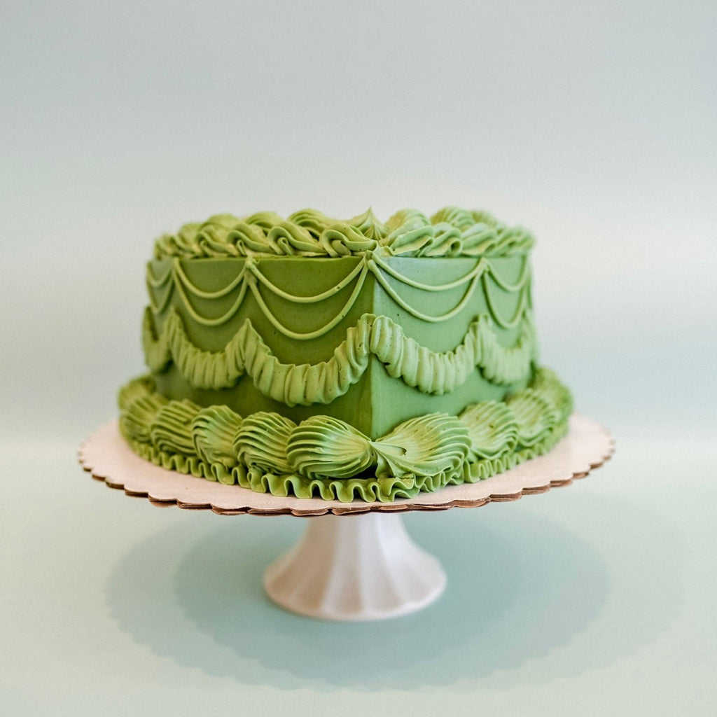 A tini bit older green heart shaped cake.  The cake has green ornate piping.
