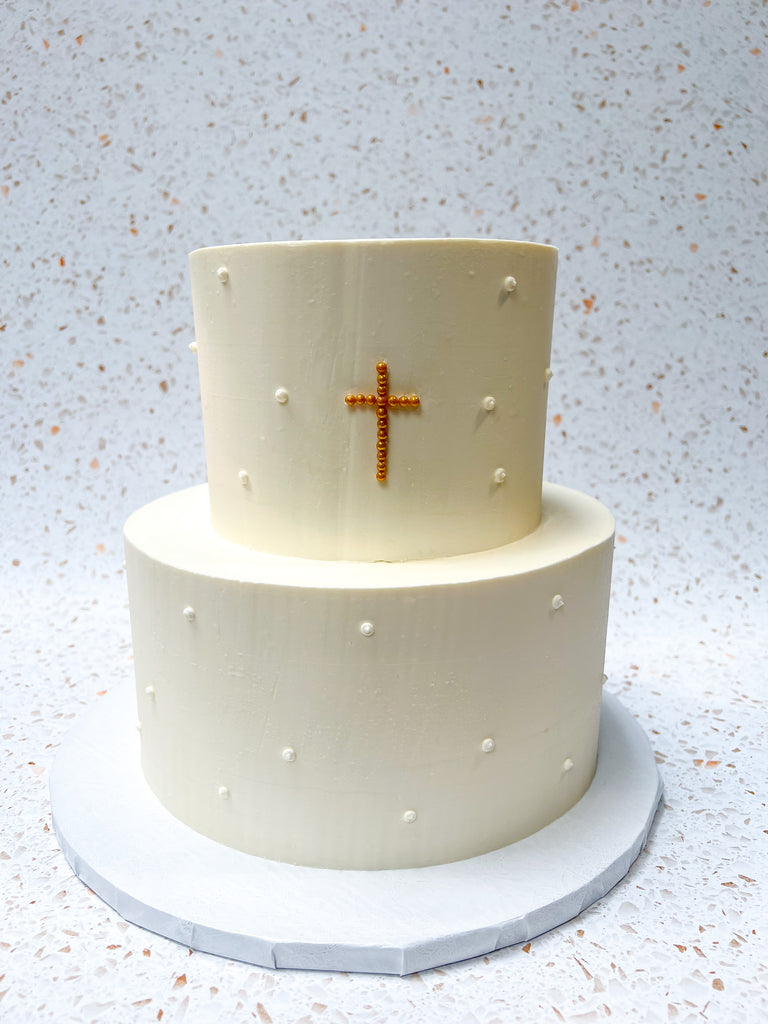 Two tiered white cake with gold cross and white pearls 