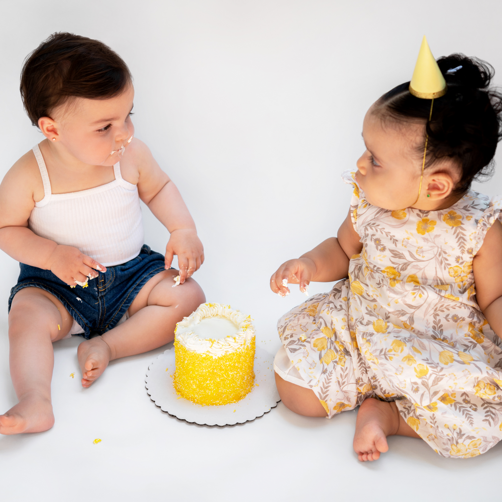 A yellow sprinkle smash cake and two one years olds smashing the cake 